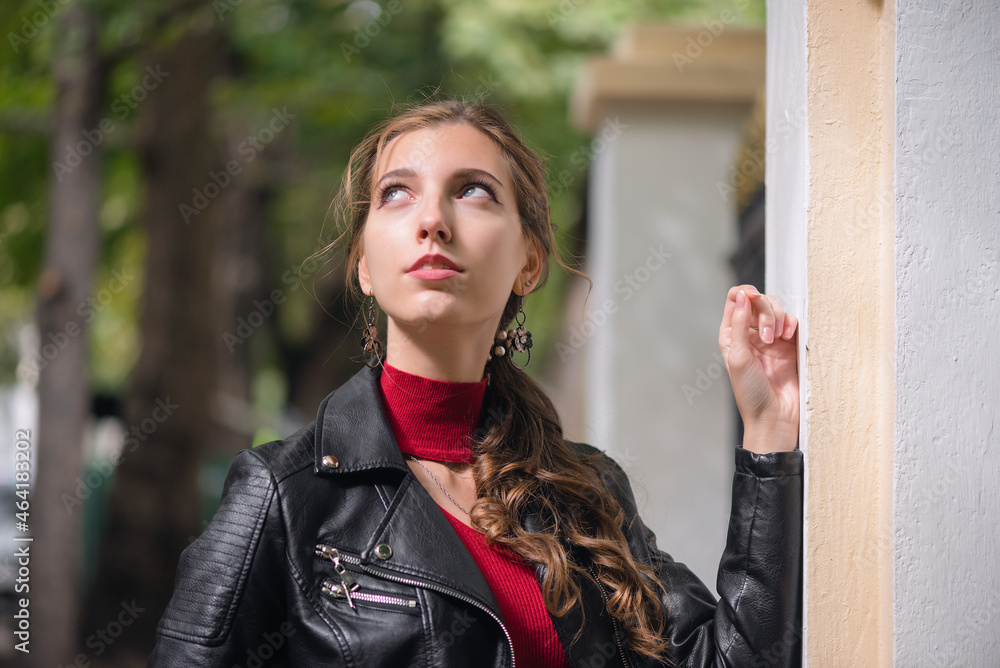 Young girl in the red dress and black leather jacket is posing on the autumn city street.