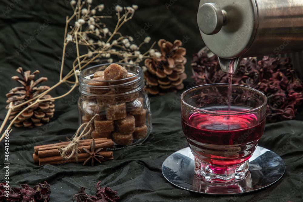 Roselle tea (Jamaica sorrel, Rozelle or hibiscus sabdariffa ) is poured from a kettle into glass cup with dry roselle and brown cane sugar cube. Healthy herbal tea rich in vitamin C and minerals. The Roselle tea (Jamaica sorrel, Rozelle or hibiscus sabdariffa ) is poured from a kettle into glass cup with dry roselle and brown cane sugar cube. Healthy herbal tea rich in vitamin C and minerals. The