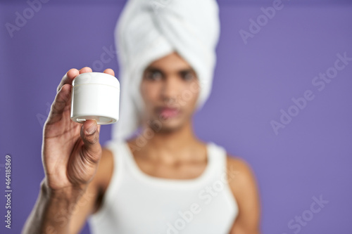 Attractive male show cream in hand bokeh portrait. Young african american man in white towel, t-shirt