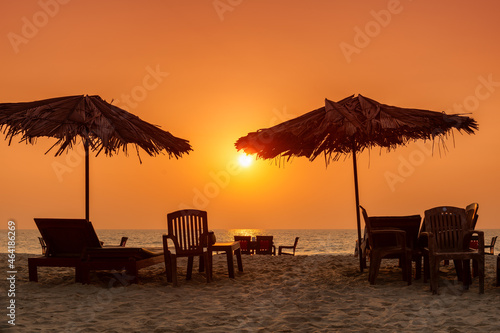 Straw umbrellas with lounge chairs at sunset on a tropical sunny beach in GOA, India photo