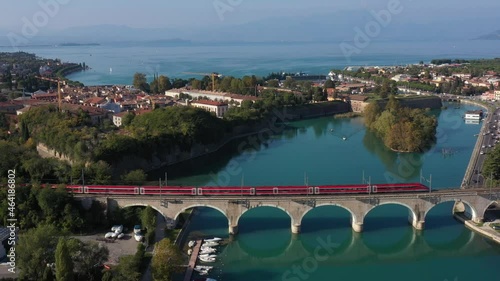 Red high-speed train on the bridge. Frecciarossa high-speed train passes an arched railway bridge over a river in the background Lake Garda Italy. photo
