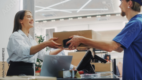 Clothing Store Checkout Cashier Counter: Retail Sales Managers Pack and Give Package Delivery Courier to Deliver Online Order. Fashion Shop Designer Brands Made Available with Online Shopping