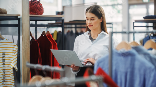 Clothing Store: Businesswoman and Visual Merchandising Specialist Uses Laptop To Create Stylish Collection. Fashion Shop Sales Retail Manager Checks Stock. Small Business Owner and Designer Works photo