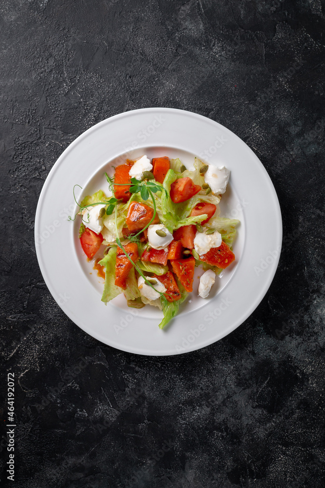 Fresh baked pumpkin salad with tomato, pumpkin seeds, Peking cabbage, feta cheese and vegetable dressing. Healthy food, vegetarian dieting, close up on dark background Fresh baked pumpkin salad with tomato, pumpkin seeds, Peking cabbage, feta cheese and vegetable dressing. Healthy food, vegetarian dieting, close up on dark background