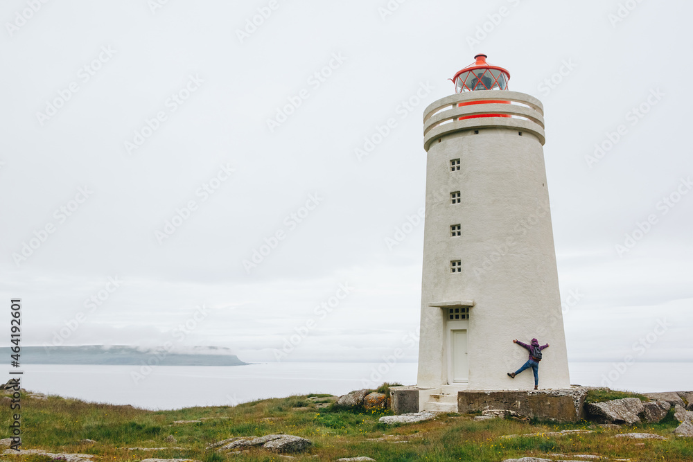 tourist in bright pink jacket have fun at the white lighthouse in Iceland