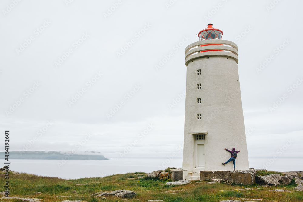 tourist in bright pink jacket have fun at the white lighthouse in Iceland tourist in bright pink jacket have fun at the white lighthouse in Iceland