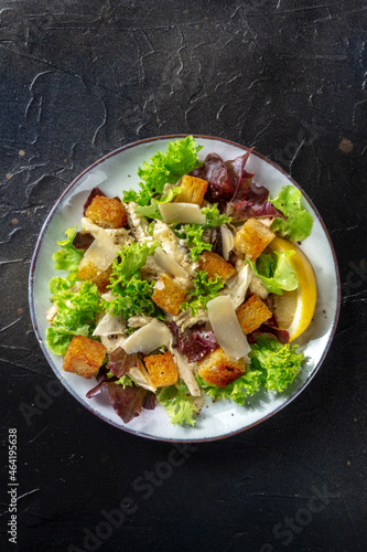 Caesar salad, shot from the top on a black background. Lettuce leaves, crispy croutons and chicken meat, with copy space