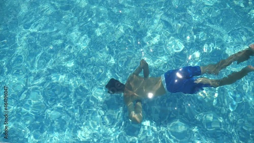 Brunet boy in shorts swimming underwater in a light-blue wading pool in slo-mo 