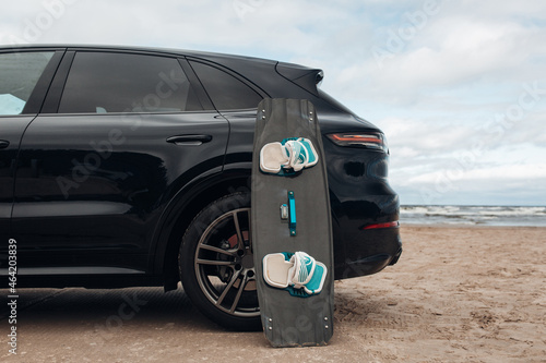 Close-up surfboard and kite equipment on sand beach near-luxury SUV car
