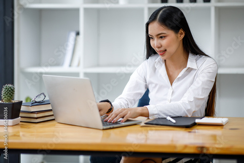 Portrait of Asian young female Businesswoman working on laptop computer doing finances,accounting analysis,report,data and pointing graph at the office.