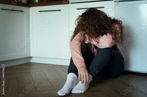 Broken young caucasian woman with hidden face sitting on floor in the kitchen