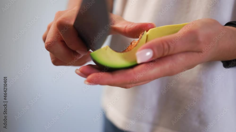 White T-shirt holds her hand green fresh firm, unripe avocado, cuts core, middle nut rind with large, uncomfortable knife. Dangerous, inconvenient use. Advertising universal kitchen utensils, products White T-shirt holds her hand green fresh firm, unripe avocado, cuts core, middle nut rind with large, uncomfortable knife. Dangerous, inconvenient use. Advertising universal kitchen utensils, products