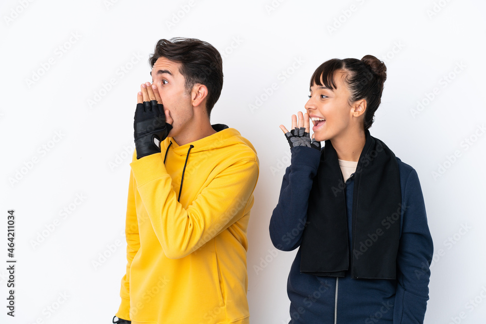Young mixed race sport couple isolated on white background shouting with mouth wide open to the lateral Young mixed race sport couple isolated on white background shouting with mouth wide open to the lateral