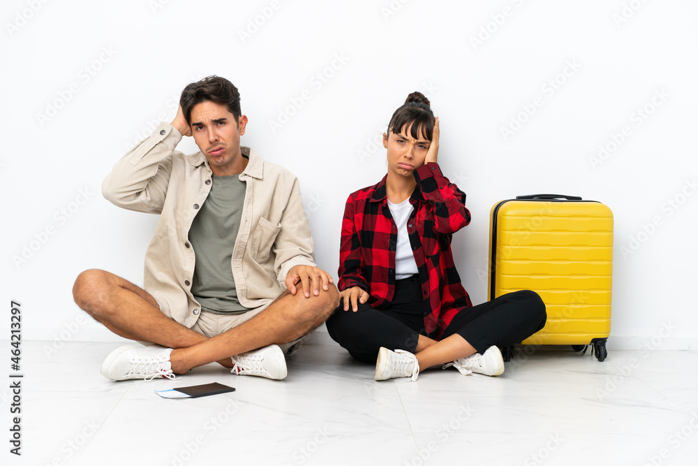 Young mixed race travelers couple sitting on the floor isolated on white background with an expression of frustration and not understanding Young mixed race travelers couple sitting on the floor isolated on white background with an expression of frustration and not understanding
