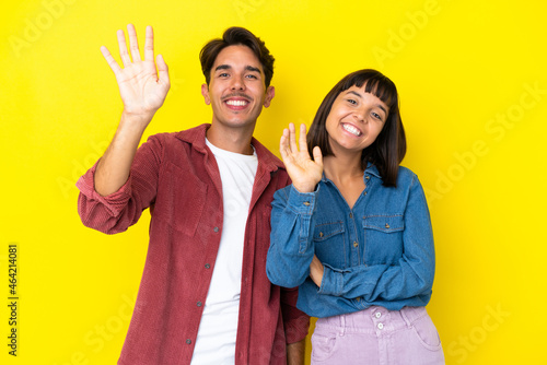 Young mixed race couple isolated on yellow background saluting with hand with happy expression