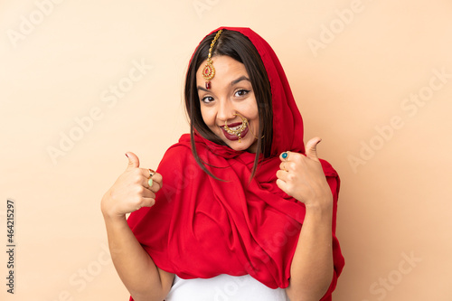 Young Indian woman isolated on beige background giving a thumbs up gesture © luismolinero
