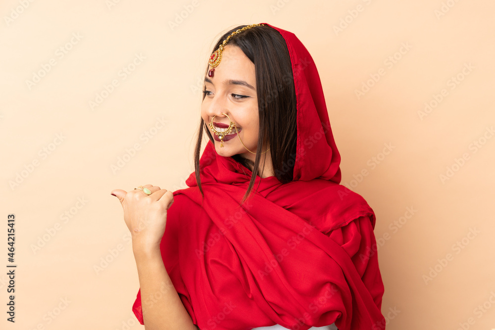 Young Indian woman isolated on beige background pointing to the side to present a product Young Indian woman isolated on beige background pointing to the side to present a product