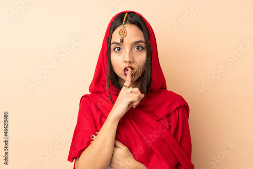 Young Indian woman isolated on beige background showing a sign of silence gesture putting finger in mouth