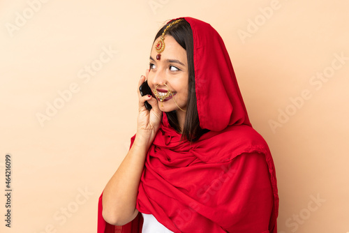 Young Indian woman isolated on beige background keeping a conversation with the mobile phone with someone