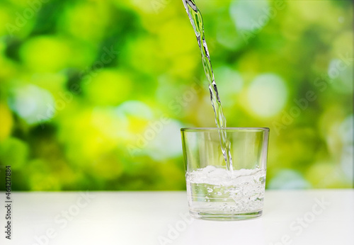 pouring pure water into a short transparent glass on the desk with a greenery background. a studio shoot of water pouring.