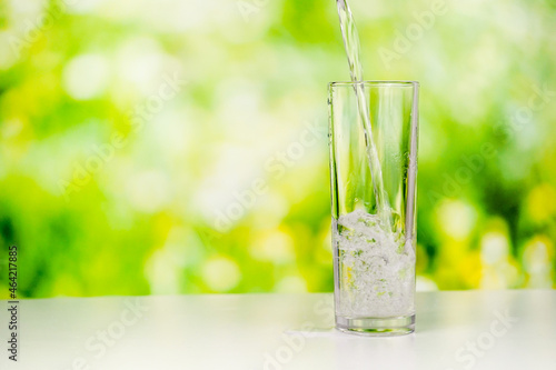 pouring pure water into a tall transparent glass on the desk with a greenery background. a studio shoot of water pouring.