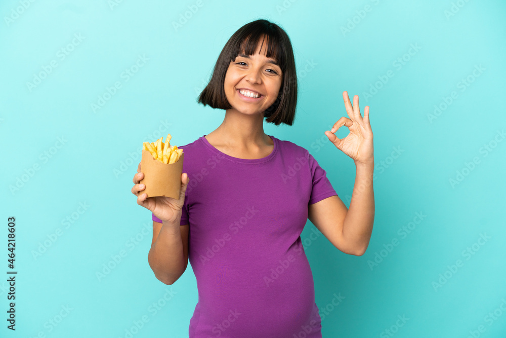 Pregnant woman holding fried chips over isolated background showing ok sign with fingers Pregnant woman holding fried chips over isolated background showing ok sign with fingers