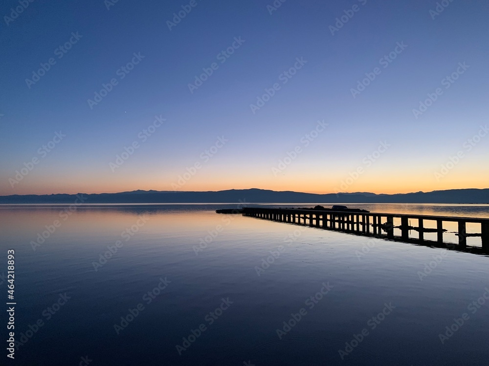 Silhouette of a long pier at the surface of the lake, sunset time, natural colors