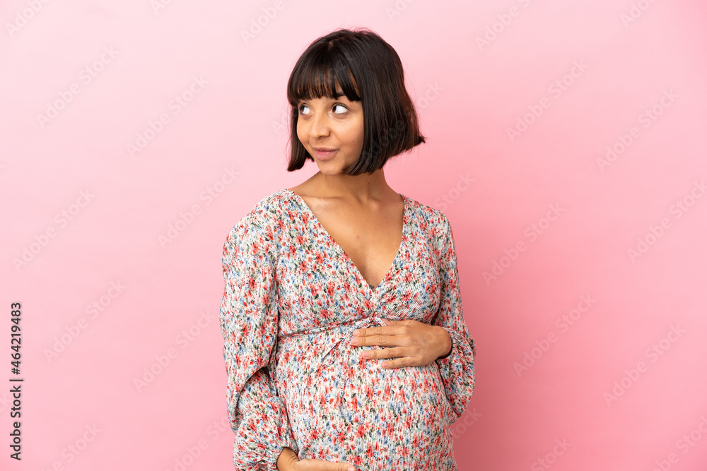 Young pregnant woman over isolated pink background having doubts while looking side Young pregnant woman over isolated pink background having doubts while looking side