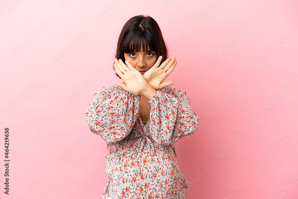 Young pregnant woman over isolated pink background making stop gesture with her hand to stop an act Young pregnant woman over isolated pink background making stop gesture with her hand to stop an act