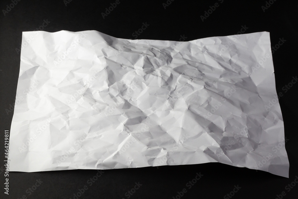 Close up of light and shadow on creases in sheet of white paper, on black background