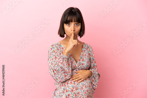 Young pregnant woman over isolated pink background showing a sign of silence gesture putting finger in mouth © luismolinero