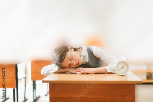 tired schoolgirl preteen with long hair in pigtails sleeps on a desk, watches.