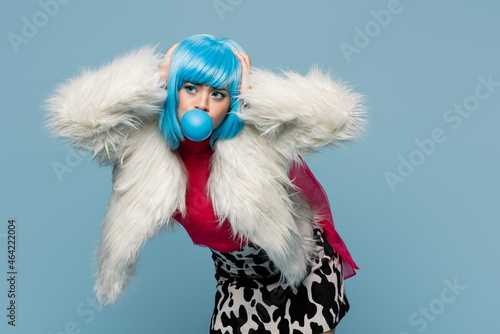 Stylish asian pop art woman blowing bubble gum and touching head isolated on blue © LIGHTFIELD STUDIOS