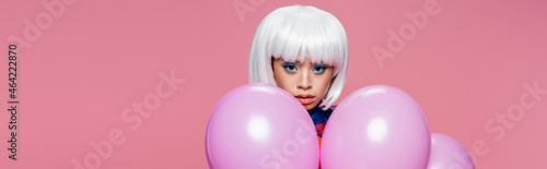 Asian woman in white wig looking at camera near balloons isolated on pink, banner © LIGHTFIELD STUDIOS