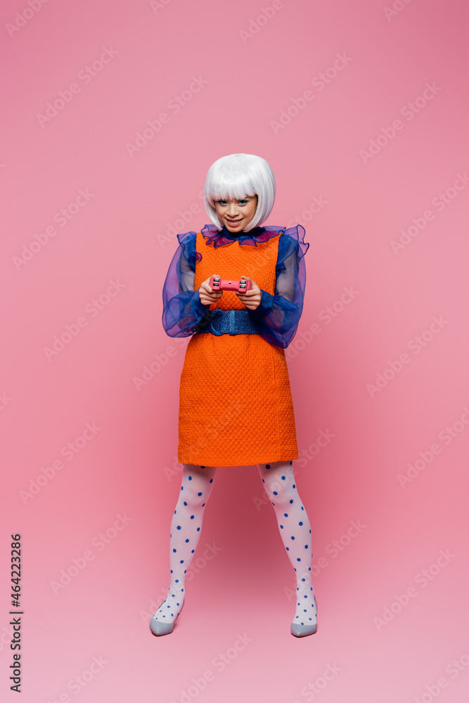 KYIV, UKRAINE - DECEMBER 10, 2020: Smiling asian pop art model holding joystick on pink background