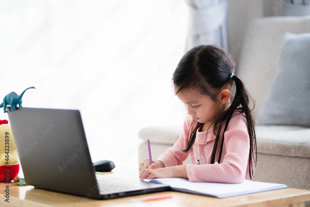 Happy asian little schoolgirl is writing and enjoy studying for online class at home, concept of technology and distance learning in the crisis situation of covid-19 pandemic around the word. Happy asian little schoolgirl is writing and enjoy studying for online class at home, concept of technology and distance learning in the crisis situation of covid-19 pandemic around the word.
