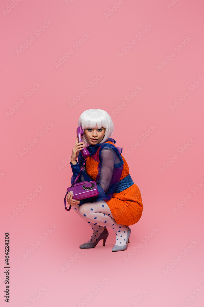 Smiling asian pop art model looking at camera while talking on telephone on pink background Smiling asian pop art model looking at camera while talking on telephone on pink background