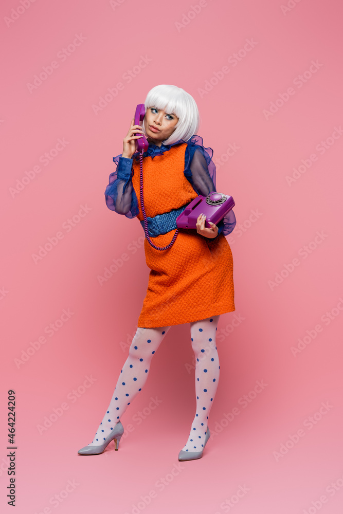Skeptical asian pop art model talking on telephone on pink background Skeptical asian pop art model talking on telephone on pink background