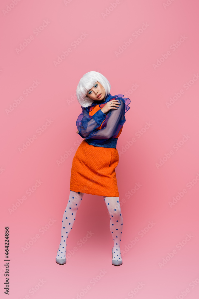Stylish asian woman in heels and white wig posing on pink background Stylish asian woman in heels and white wig posing on pink background