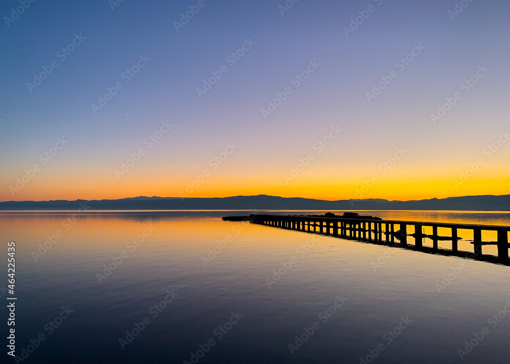 Silhouette of a long pier at the surface of the lake, sunset time, natural colors