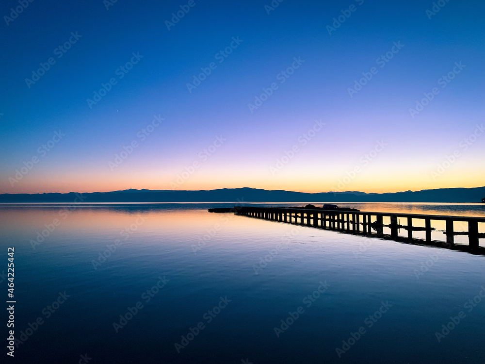 Silhouette of a long pier at the surface of the lake, sunset time, natural colors