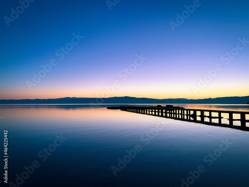 Silhouette of a long pier at the surface of the lake, sunset time, natural colors © Oksana