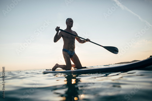 Senior man paddling board on sunset sea
