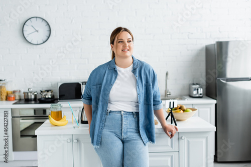 Happy woman with overweight standing near kitchen table with cellphone and food
