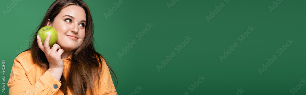 Pretty brunette woman with overweight holding fresh apple isolated on green, banner Pretty brunette woman with overweight holding fresh apple isolated on green, banner