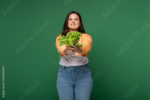 Fotografía Smiling woman with overweight holding lettuce isolated on green