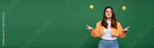 Cheerful woman with overweight throwing apples isolated on green, banner © LIGHTFIELD STUDIOS
