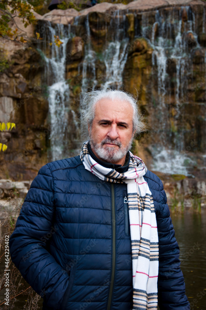 senior grizzled man in autumn jacket and scarf on waterfall nature background senior grizzled man in autumn jacket and scarf on waterfall nature background