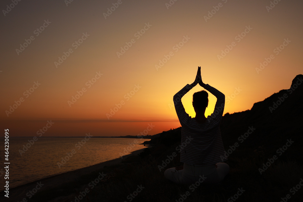 Woman meditating near sea at sunset, back view. Space for text