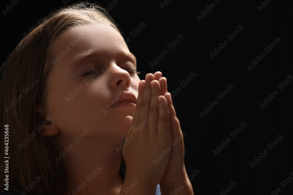Cute little girl with hands clasped together praying on black ...